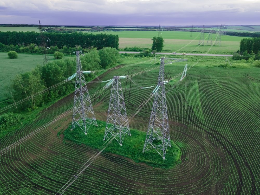 High voltage electric power tower in a green agricultural landscape at beautiful sunset