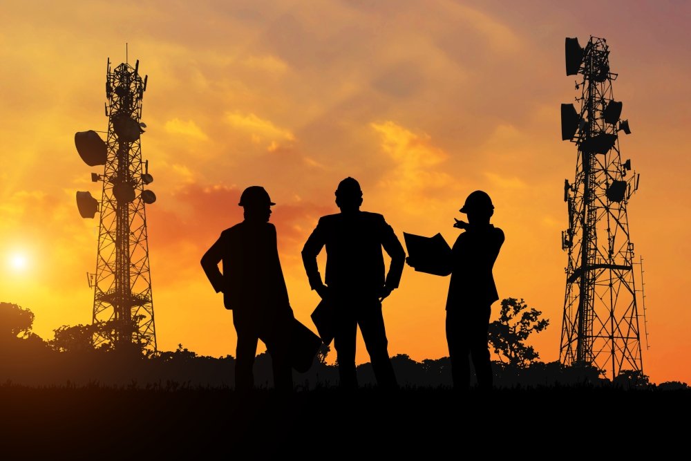 Silhouette of the engineers look at the telecommunication poles planned to be built at sunset time