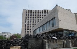 Exterior of a brutalist concrete building, surrounded by a large pile of tires. 