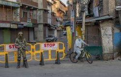 A Kasmiri man on a bicycle rides past a barricade guarded by a soldier.