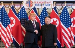 Donald J. Trump stands next to Kim Jong Un as they shake hands and pose in front of U.S. and North Korean flags