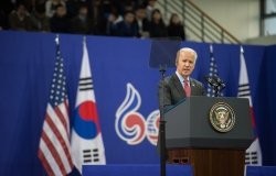Joe Biden stands at a podium delivering a speech in front of U.S. and South Korean flags