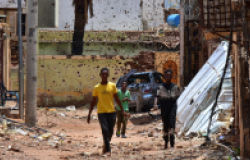 Young people walk along a street marked by destruction. A bloody power struggle has been raging in Sudan for more than 16 months, triggering a refugee crisis. Mudathir Hameed/picture-alliance/dpa/AP Images.