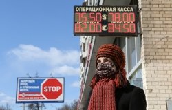 A woman stands in front of a sign displaying the ruble's exchange rate
