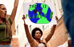Low angle view of a woman carrying a banner with a “There Is No Planet B” inscription while protesting with a crowd of activists against climate change