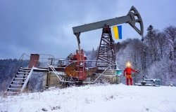 A working engineer at an oil and gas development of an old field checks the operation of mechanisms and control systems in the mountains after a winter in early spring. Flag of Ukraine yellow-blue.